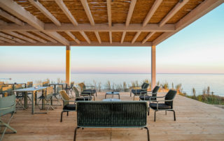Tavolo in legno sotto un pergolato con vista sul mare cristallino, in un contesto architettonico mediterraneo e rilassante